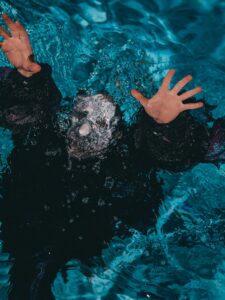 Person underwater with hands reaching up, depicting a struggle or emergency situation in water.